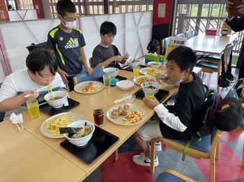 昼食のラーメンを食べている男の子4名の机の上にはお盆にのせた料理が置かれている楽しそうな食事の様子を写した写真