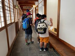 リュックを背負った児童たちが日新館の木造廊下で壁際にある展示をのぞき込んで見学している様子の写真