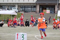 番号は「3」と大きく書かれたオレンジ色のビブスを着て赤い帽子をかぶった男子児童が全力で走っている写真