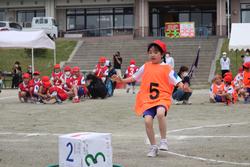 番号は「5」と大きく書かれたオレンジ色のビブスを着て赤い帽子をかぶった女子児童が全力で走っている写真