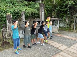 後ろに石碑が並んでいる飯盛山で見学中の児童たちが、手を額に当てて遠くを見渡すポーズをしている様子を写した写真