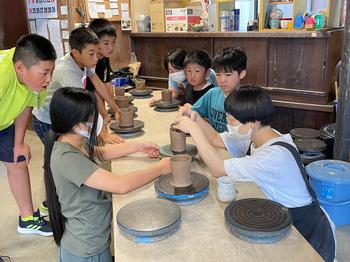 子供達が見ている中、講師の女性が土を触って形を作っているゆのみづくり体験での写真