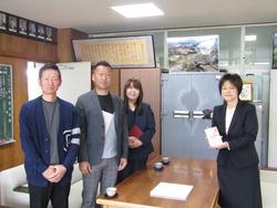 応接セットの左側に男性2人と女性、右側に封筒を持った女性が立って写した記念写真