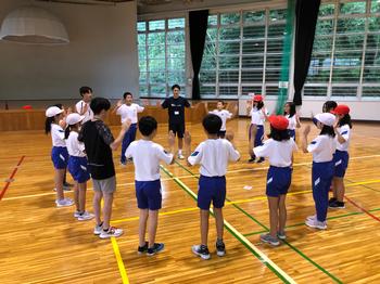 体操服姿の生徒たちが体育館で円になり両手をあげている写真