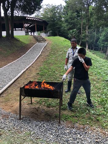 男性に見守られながら、一人の男の子が火が付いた炭の上で焼き板を焼いている写真