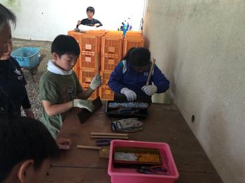 壁際に設置された机の上で数名の子供たちが板を金ブラシできれいに磨いている写真