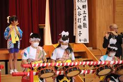 和太鼓を演奏する衣装を着た子どもたちと、笛を吹く大人が舞台で郷土芸能を披露している写真