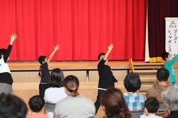 舞台の前で子どもたちが手を高く上げてダンスを披露し、観客がその様子を見守っている写真