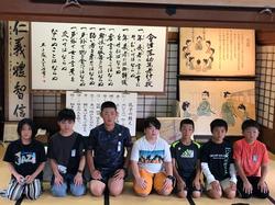 日新館の和室で、七人の児童が掛け軸や歴史的な資料の前に正座して記念写真を撮っている様子の写真