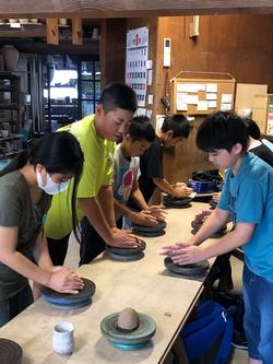 木製の長机の上に児童達が並び、それぞれが両手で粘土を包み込むように形を整えている慶山焼き体験の様子の写真