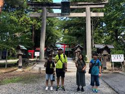 リュックを背負った4人の児童が大きな石の鳥居の前に並んで立っている写真