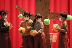 茶色い服と動物の耳をつけた子どもたちが、手作りの果物を手にして舞台の木のそばに立っている写真