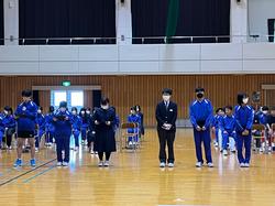 体育館に並べられた椅子に座っている生徒たちの前に、6人の生徒が間隔をあけて横一列に並んでいる写真