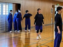 体育館でジャージ姿の女子生徒たちが立って順番を待っている様子の部活時の写真