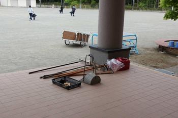 手前に作業に使用する道具が置かれ、運動場には3名が一輪車を押して作業をする様子の写真