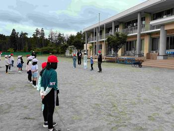 運動場で各班の代表者が感想発表を行い、他の児童達が立って聞いている様子の写真