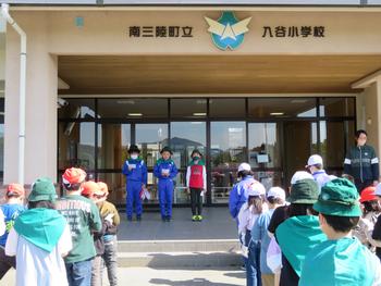 南三陸町立入谷小学校の玄関前で、整列した子どもたちの前に3人の児童が立ち、発表をしているようすの写真