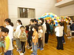 体育館の入口に児童がフラワーペーパーで造られたアーチを持ちアーチを通って新一年生と保護者の方が入場している写真