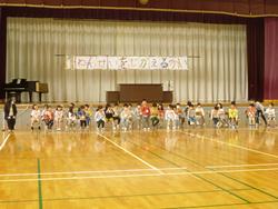 体育館の舞台の下に並べられた椅子に新一年生が座り中央で1人の新一年生が立って自己紹介をしている写真