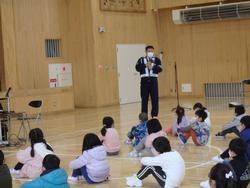 三陸警察署の警察官がマイクスタンドの前に立ち、床に座っている子どもたちに向けて安全について話している写真