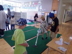 バンダナを着けた生徒たちが室内の緑のマットの上で掃除機を使って清掃活動を行っている写真