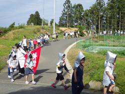防災頭巾を被った生徒たちが舗装された道を整列しながら歩いて避難訓練をしている様子の写真