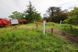 緑の草が生い茂る広場の中に赤い杭とロープで囲まれ中央には白い標柱が立っている田束山経塚群の写真