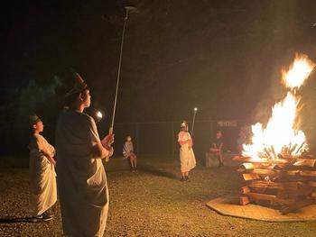 キャンプファイヤーの周りに棒を持った児童が数名立っている写真