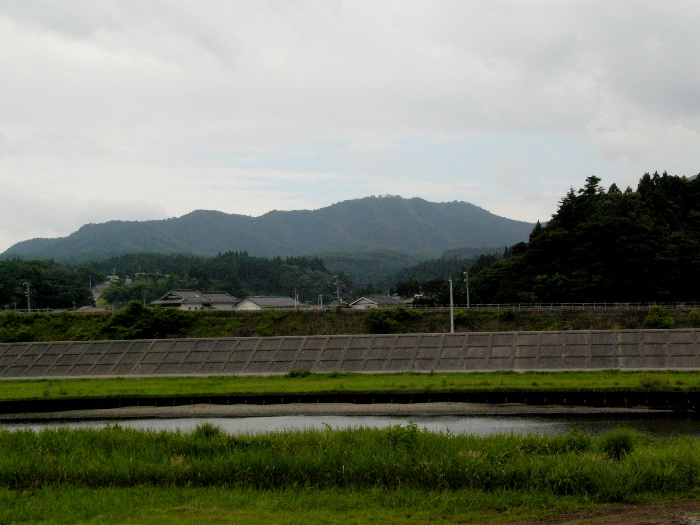 曇り空の下、川の向こうに広がる山並みと集落が見える静かな風景の写真
