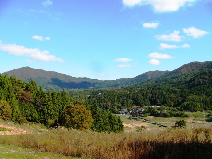 秋の草原と緑の森に囲まれた山あいの田園風景の写真