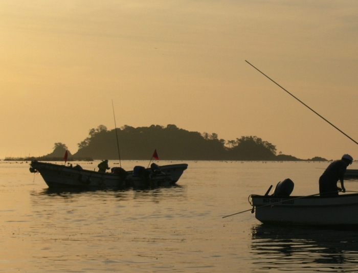 朝やけの海の上を釣りや作業をする漁師たちとその小舟がシルエットになった海の写真