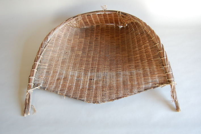 三角形の形で左右に持ち手が付いた藁で編まれた農作業用の箕の写真