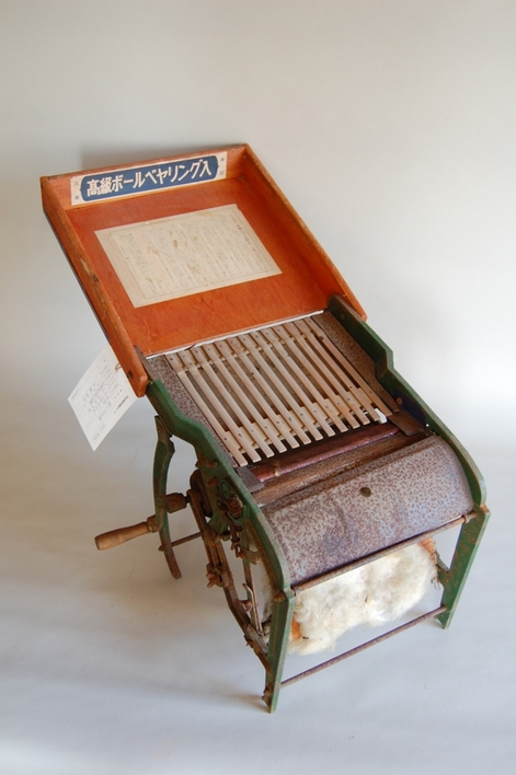 金属と木でできた手動式で傾斜のついた昔の毛羽取り機の写真