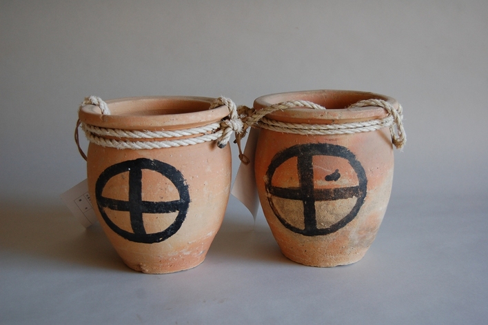 側面に円形と十字の模様が描かれた土でできた小さな壺が2つ並び、口に縄が巻かれているタコ壷の写真