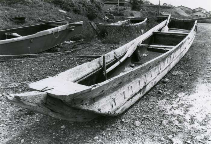 L字型にくりぬいた二本の丸太で作られた細長い木造の舟カナオレカッコが浜辺に置かれている白黒写真
