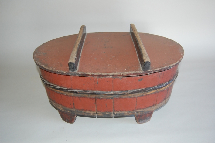 全体が朱色で上に持ち手のような棒が2本付いた蓋があり、樽に足がついた楕円形の「ほげえ」の写真