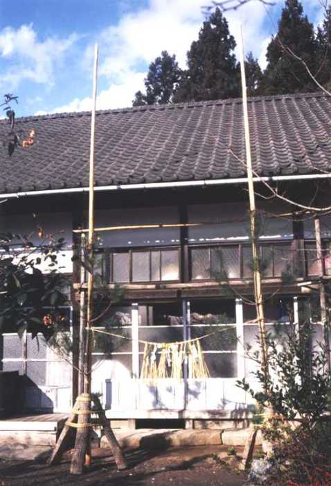 日本の伝統的な木造家屋の玄関前に、門松やしめ縄飾りが設置されて正月を迎える準備が整えられている様子を写した写真