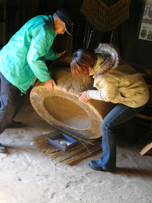 二人の人が臼伏せの大きな木製の臼を傾け、中のお供え餅を取り出そうとしている写真