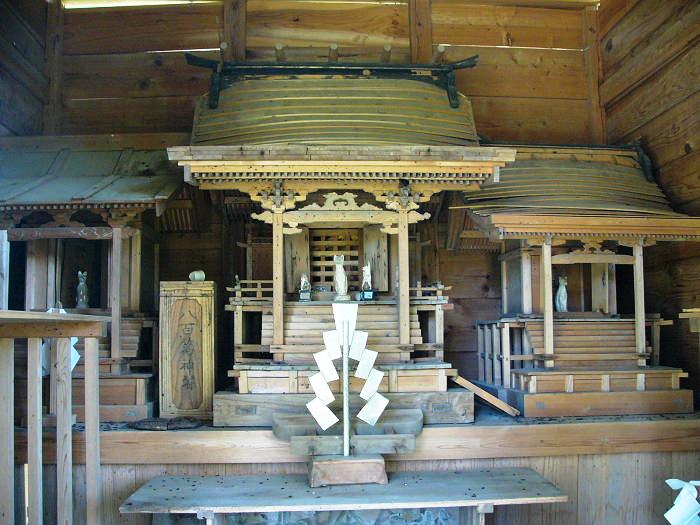 木造の社殿内に三つの精巧な祠が並び、中央に紙垂をつけた神道の装飾が置かれている写真