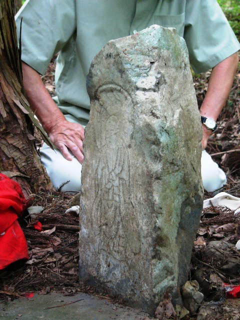 周囲に落ち葉が落ちている地面に石碑が立ち、表面には袈裟を着た人物のようなものが彫られている金掘り人夫供養の地蔵の写真