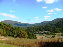 秋の草原と緑の森に囲まれた山あいの田園風景の写真
