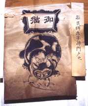 紙の上部に「御猫」という文字があり、中央にはネズミをくわえた猫の絵が墨で力強く描かれている御札の写真