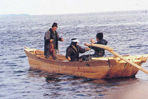 水上で木造の合木船に立っている人とオールを持って座る2人が乗っている写真