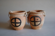 側面に円形と十字の模様が描かれた土でできた小さな壺が2つ並び、口に縄が巻かれているタコ壷の写真