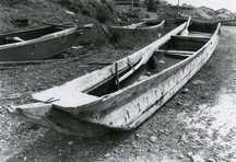 L字型にくりぬいた二本の丸太で作られた細長い木造の舟カナオレカッコが浜辺に置かれている白黒写真