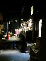 窓から太陽光が差し込んだ薄暗い土間にガスコンロや冷蔵庫などの台所道具が置かれた昔の炊事場の写真