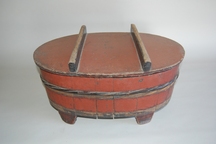 全体が朱色で上に持ち手のような棒が2本付いた蓋があり、樽に足がついた楕円形の「ほげえ」の写真