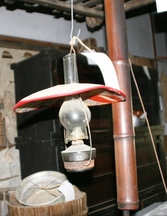 木製のタンスが設置された室内に、赤い縁の笠が付いたガラス製のランプが天井から吊るされた写真