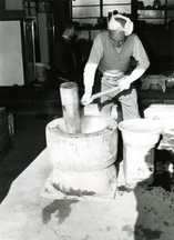 頭にタオルを巻いた男性が大きな臼で杵を使って餅をついている白黒写真