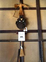 土壁と木枠の家屋内に、藁の飾りや紙垂とともにカマドの神ともいわれる「かま神さま」の面が祀られている写真